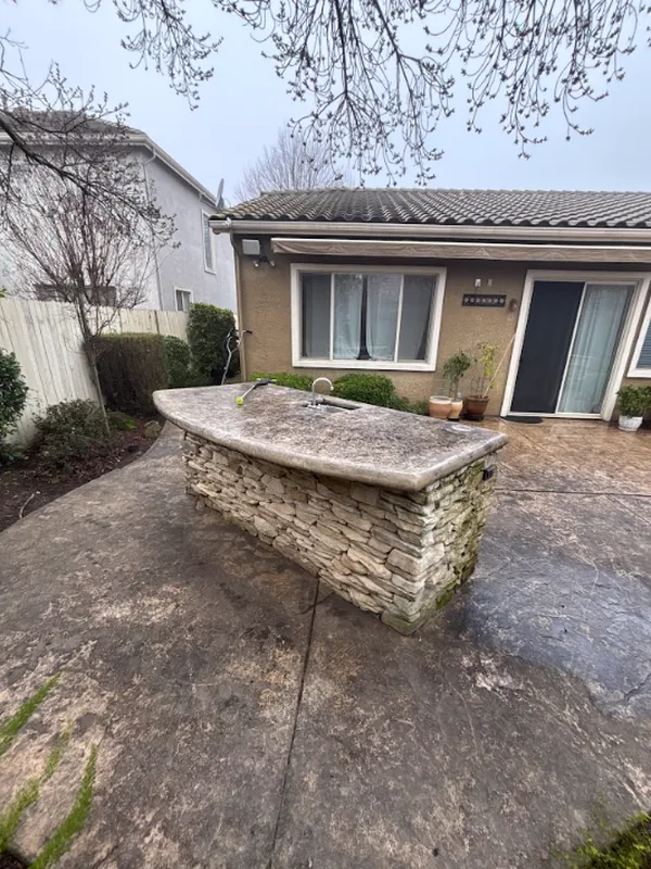 Dark surface buildup on the stamped-concrete patio around a stone outdoor bar